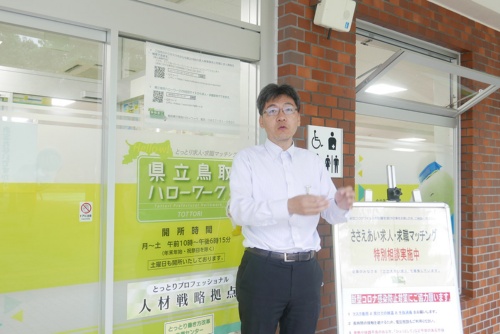 JR鳥取駅にある「鳥取県立 鳥取ハローワーク」の前で、副業・兼業プロジェクトについて語る鳥取ハローワーク課長補佐の細田浩一氏。「県立ハローワークの事業には、女性、若者、ミドル・シニアの就職支援等5つの柱がありますが、その中の1つの柱が企業の人材確保を支援することで、その中にプロフェッショナル人材事業というものを位置づけています」(写真:高山和良)