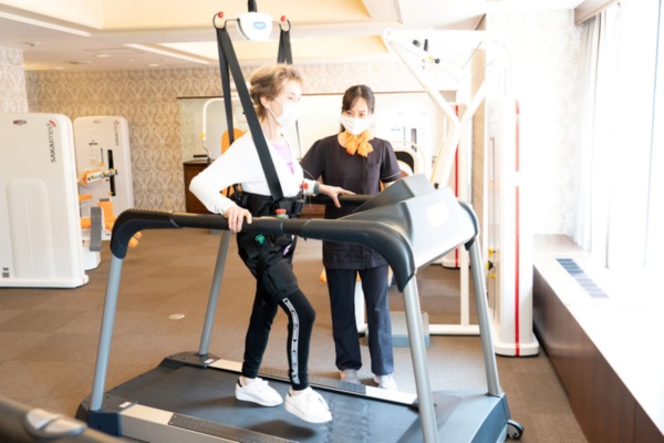 天井懸下式の支持装置を備えたトレッドミル「Pウォーク」。転倒防止装置や安全装置を備える。0.2km/hといったゆっくりスピードで練習を始める。このトレッドミルで2km歩けるようになった時点で外出訓練リハビリを開始する(撮影:大亀 京助)