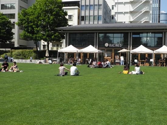 (写真2)カフェレストラン「RACINES FARM TO PARK」前の芝生広場。生育状況は良好で、一面の緑が美しい。屋外のテラス席で飲食する来園者も多い(写真:茂木俊輔)